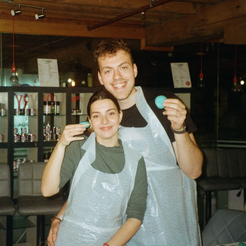 Doni and Niki, founders of Doki’s Kitchen, smiling together while holding macarons during a cooking class